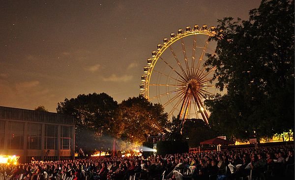 Viele Personen auf Stühlen bei der swa Kurzfilmnacht 2024. Im Hintergrund sind Bäume und ein Riesenrad