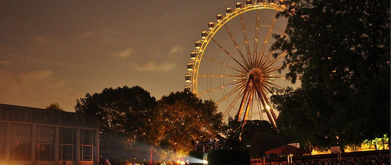 Viele Personen auf Stühlen bei der swa Kurzfilmnacht 2024. Im Hintergrund sind Bäume und ein Riesenrad