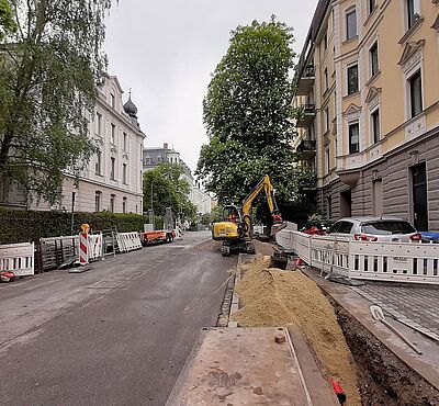 Eine Baustelle am Straßenrand. Links und rechts sind Gebäude.