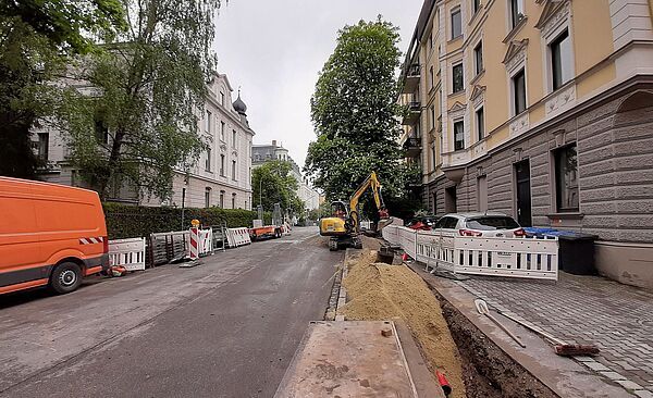 Eine Baustelle am Straßenrand. Links und rechts sind Gebäude.