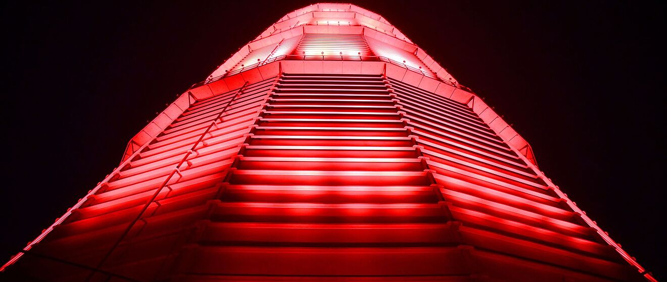Rot beleuchteter großer Scheibengasbehälter. Weiterverlinkung auf Night of Light Newsartikel