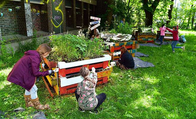 Bild von Kindern, die Hochbeete aus Paletten bunt anmalen