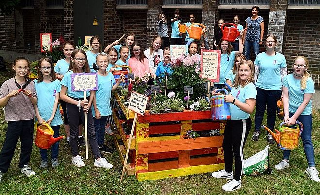 Schülerinnen, die an einem Urban Gardening Projekt der Mädchenrealschule Sankt Ursula in Augsburg beteiligt sind stehen zusammen vor einem selbstgebauten Hochbeet aus Paletten welches in zusammenarbeit mit den swa entstanden ist.