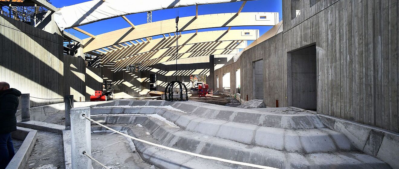 Baustelle des neuen Elefantenhauses mit Felsvorsprüngen im Vordergrund. Ein Kran legt Dekorierung ab. Im Hintergrund befinden sich weitere Geräte zur Durchführung der Bauarbeiten.