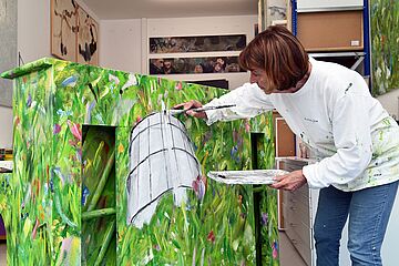 Frau malt Klavier mit verschiedenen Grün tönen an und dem Gaskessel in der Mitte. - Beim anklicken wird das Bild vergrößert.