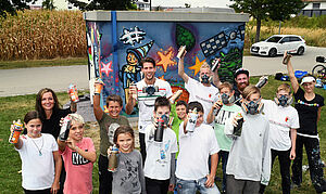 Fabian Giefer steht mit Kindern an einer Straße. Alle halten Graffiti-Dosen in die Luft.