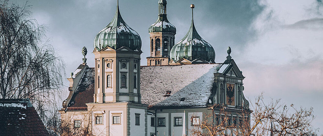 Augsburger Rathaus mit Schnee bedeckt. Im Vordergrund befinden sich Bäume.
