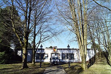 Ein Haus mit dem Augsburger Stadtwappen zwischen kahlen Bäumen. Ein Fahrzeug steht in der Mitte. - Ein Klick auf das Bild führt zur vergrößerten Fotoansicht.