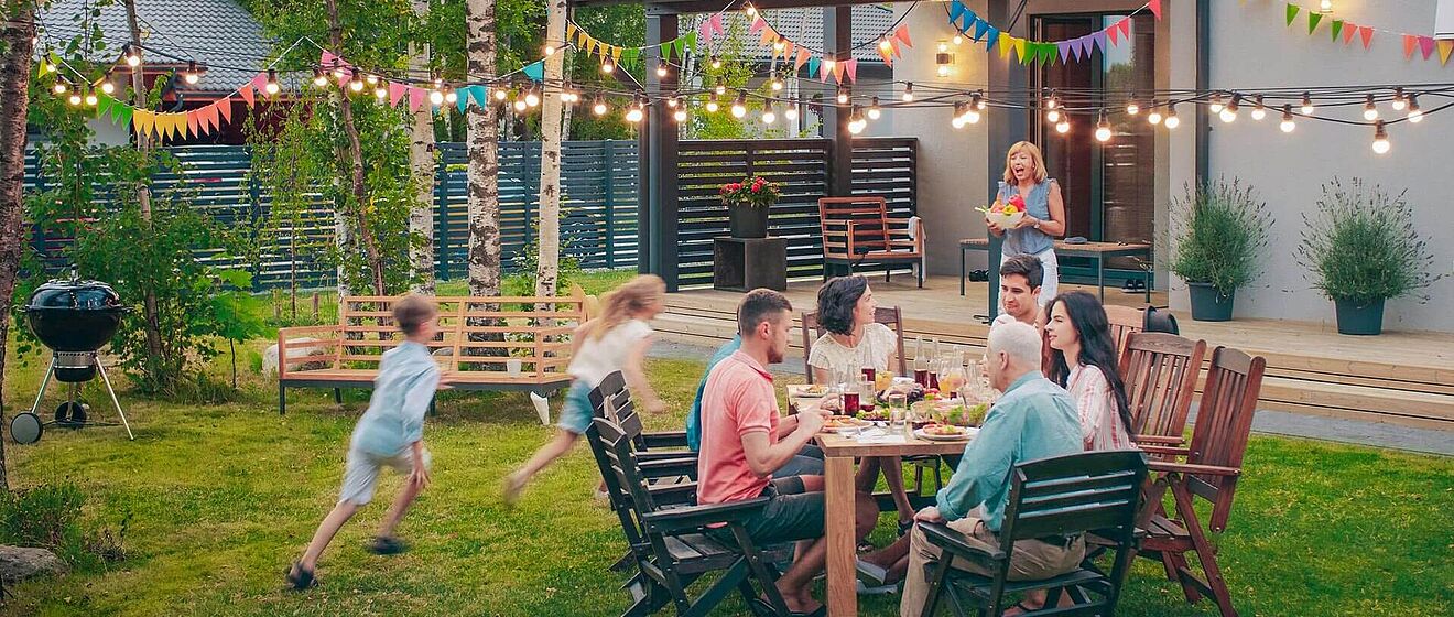 Menschen sitzen draußen im Garten auf Gartenmöbel während zwei Kinder spielen.