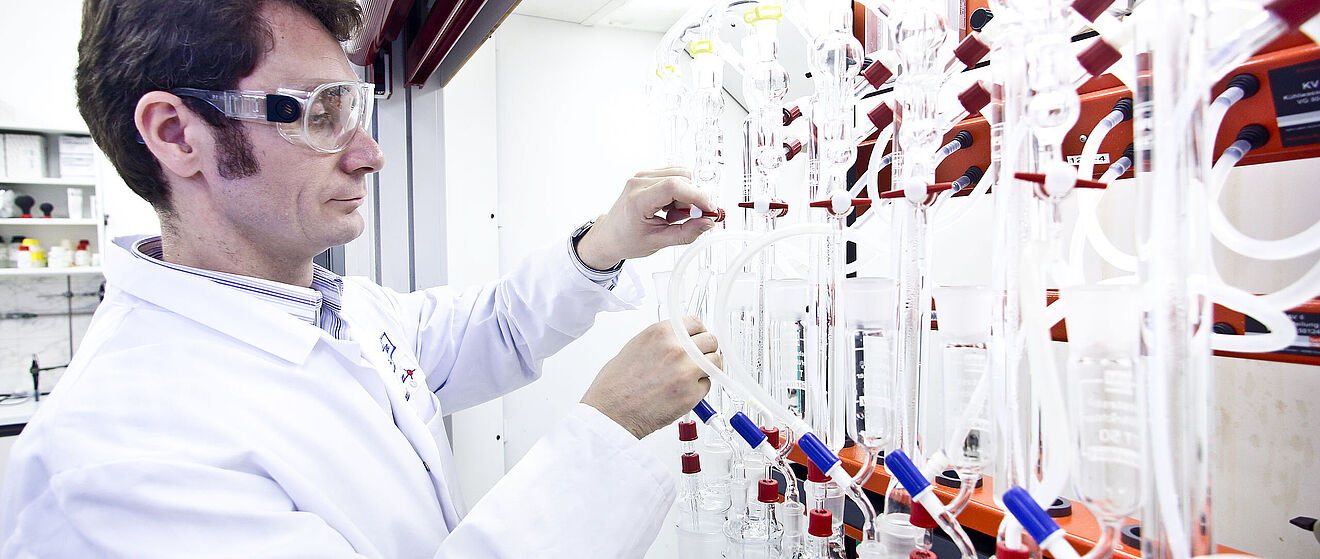 Ein Mann mit Schutzbrille und Weißer Kleidung testet in einem Labor die Wasserqualität.