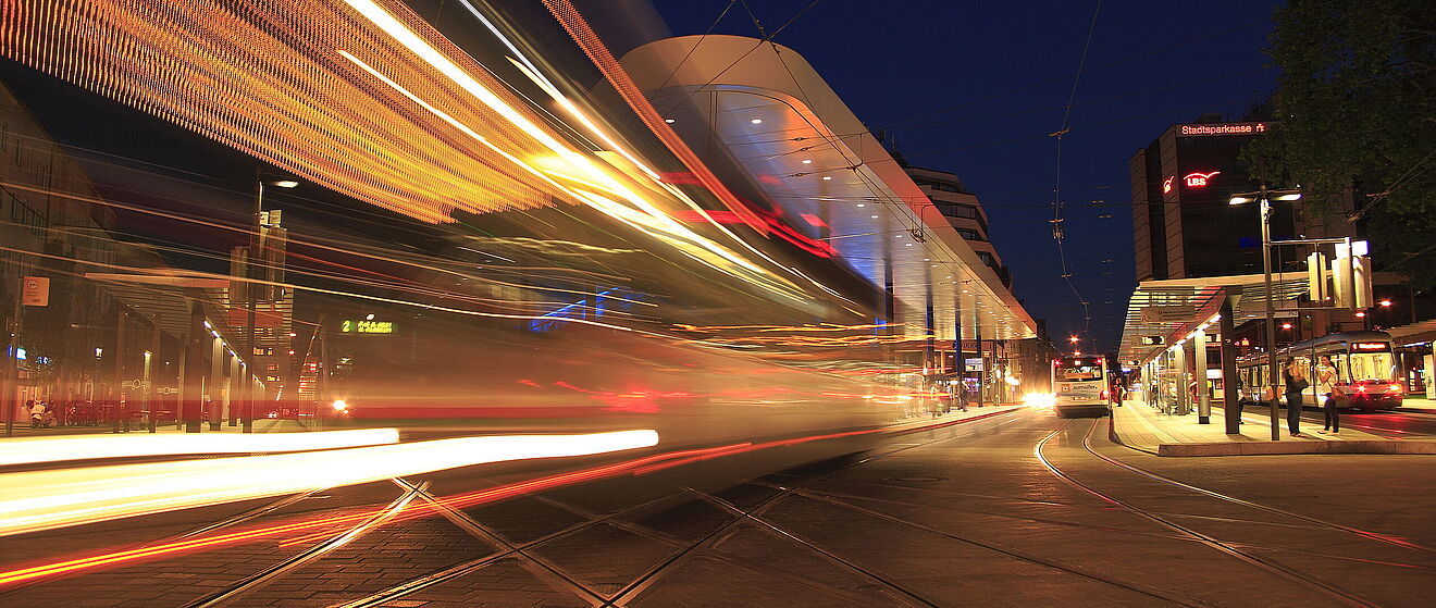 Haltestelle am Königsplatz bei Nacht. Links befindet sich die verschwommene Silhouette einer vorbeifahrenden Straßenbahn.