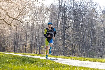 Triathlet Lukas Stahl mit swa Kappe läuft auf einem Weg im Wald