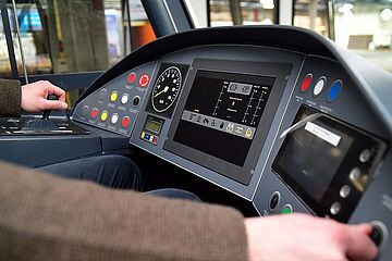 Innenansicht der Fahrerkabine in Bedienung eines Mannes welcher beide Hände auf verschiedenen Hebeln hat. - Beim anklicken wird das Bild vergrößert.