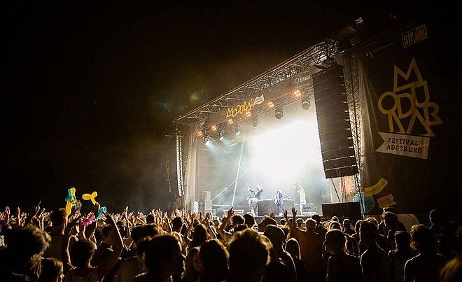 Ein LIVE-Musik-auftritt an einem vergangenen Modular-Festival in Augsburg. Die Bühne wird von Lichtern bestrahlt und eine große Menge von Menschen stehen davor.