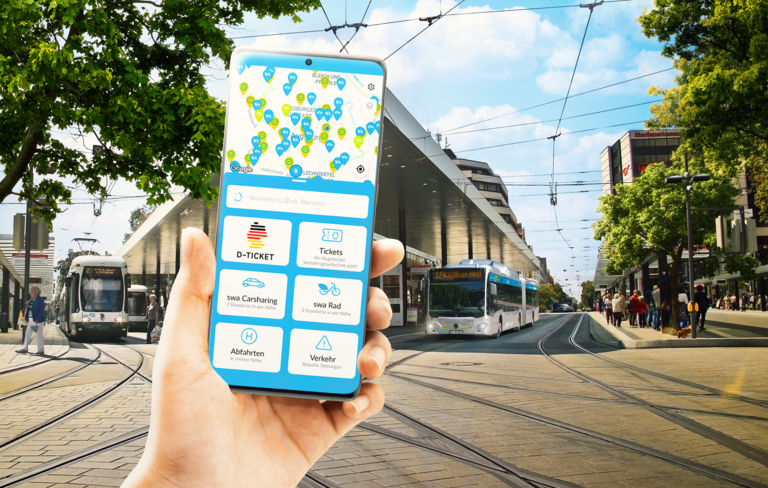 Ein Hand hält ein Smartphone mit der swa Mobil App. Im Hintergrund ist die Augsburger Haltestelle Königsplatz zu sehen.