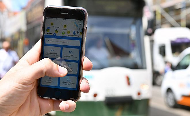 Nahaufnahme von einer Hand, welche ein Handy mit geöffneter swa Mobil-App hält. im Hintergrund eine swa Straßenbahn.