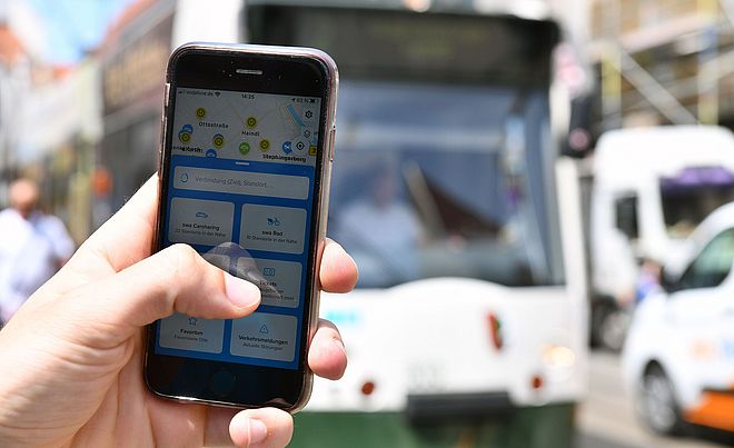 Nahaufnahme von einer Hand, welche ein Handy mit geöffneter swa Mobil-App hält. im Hintergrund eine swa Straßenbahn.