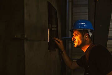 Mann mit Helm schaut in den Ofen eines Biomasse Heizkraftwerks