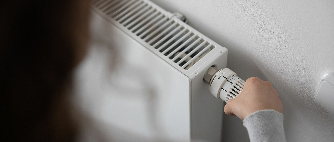 Person dreht an einer Heizung. 