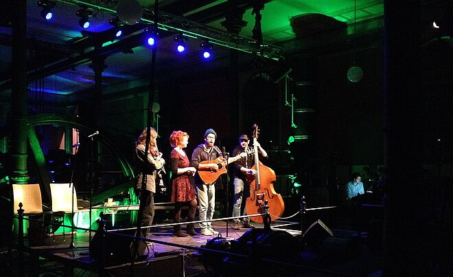 Zwei Frauen und zwei Männer stehen mit Geige Gitarre und Kontrabass auf einer Bühne.