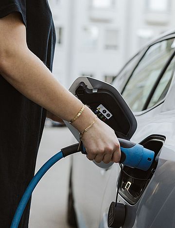 Eine Person verbindet ein Elektroauto mit einem Ladekabel an einer Ladestation.
