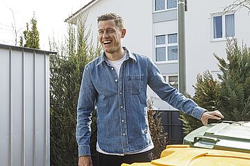 Alfred Finnbogason steht an Mülltonnen und lächelt. - Ein Klick auf das Bild führt zur vergrößerten Fotoansicht.
