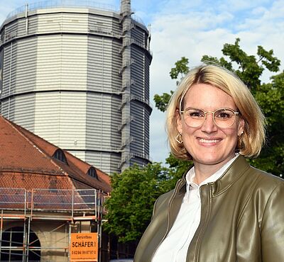 Eine lächelnde Frau rechts, links im Hintergrund ist das Gaswerk zu sehen.
