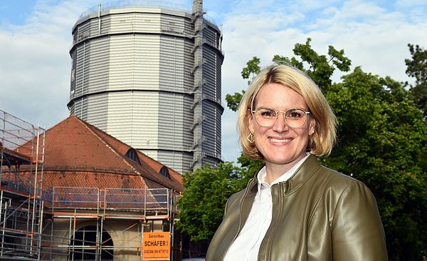 Eine lächelnde Frau rechts, links im Hintergrund ist das Gaswerk zu sehen.