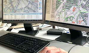 Schreibtisch mit einer Tastatur und zwei Bildschirmen auf denen Stadtpläne sind. Link zu einem Pop-Up mit Informationen zu Netzmodellberechnungen