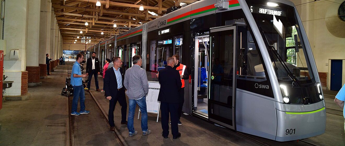 Mehrere Personen stehen vor der Straßenbahnlinie 5 in einem Straßenbahnhof