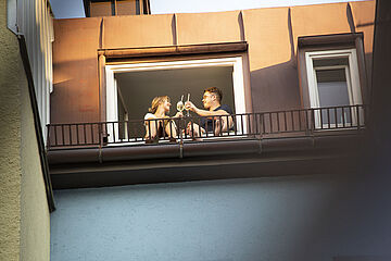 Frau und Mann stoßen vor ihrem Fenster an. - Beim anklicken wird das Bild vergrößert.