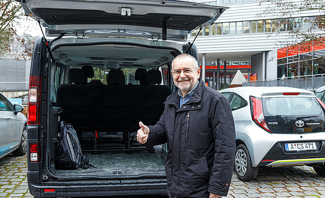 Mann steht vor Carsharing-Van mit geöffneter Heckklappe und zeigt einen Daumen nach oben