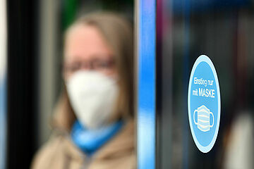Frau steht mit Maske in einer Bustür