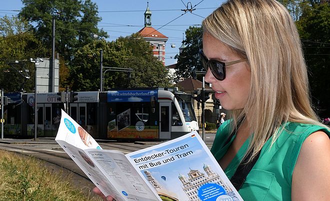 Frau mit Sonnenbrille schaut in ein Programmheft der Entdeckertour. Im Hintergrund ist eine Straßenbahn zu sehen.
