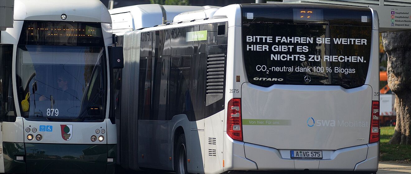 Ein Bus und eine Straßenbahn der swa stehen nebeneinander an einer Haltestelle.
