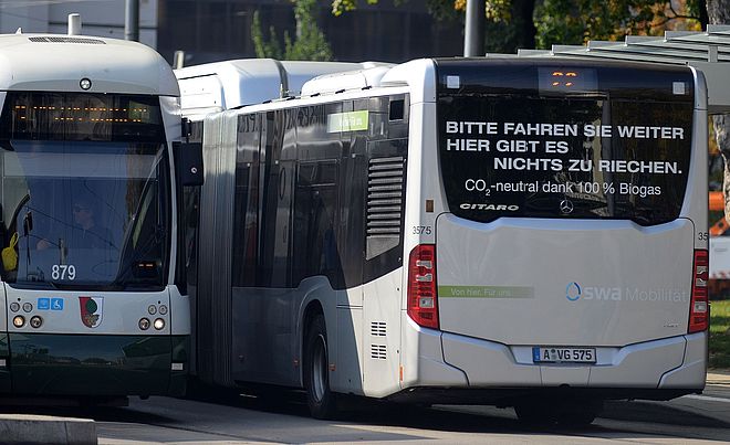 Ein Bus und eine Straßenbahn der swa stehen nebeneinander an einer Haltestelle.