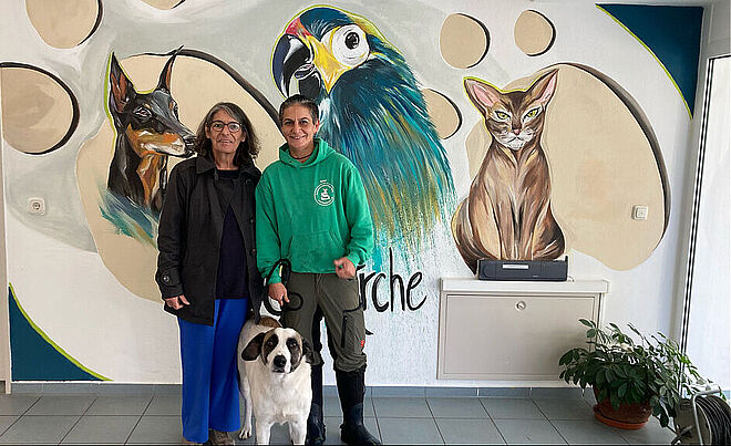 Zwei Personen stehen vor einem Tiergemälde und halten einen Hund an der Leine.