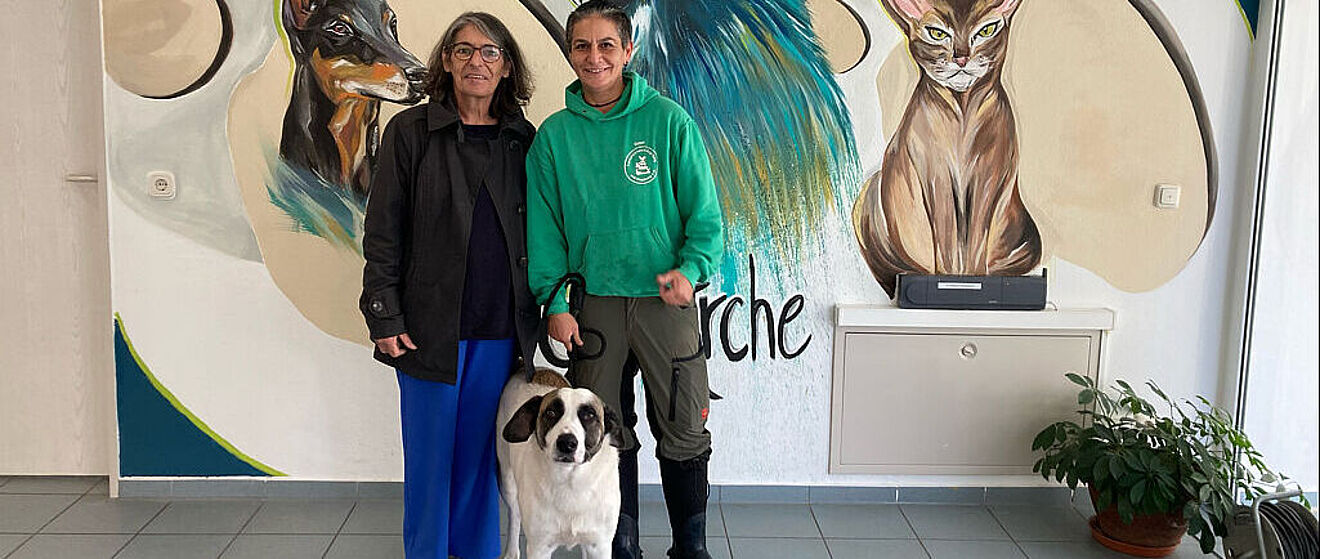 Zwei Personen stehen vor einem Tiergemälde und halten einen Hund an der Leine.