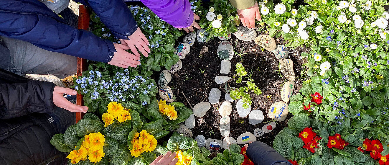 Kinder bauen ein Peace-Zeichen aus Steinen in ein Blumenbeet