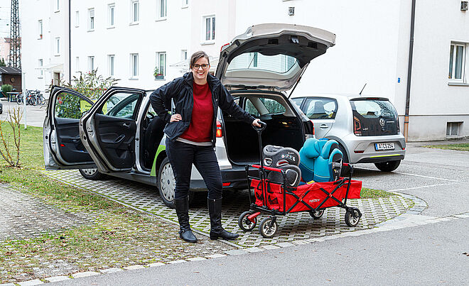 Frau steht mit Buggy vor einem Carsharingauto mit geöffneter Heckklappe