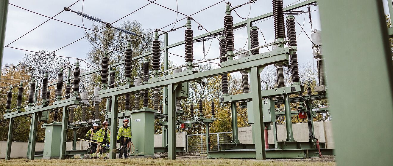 Drei swa Netze Mitarbeiter mit Schutzausrüstung und Werkzeug laufen auf der Netzeanlage