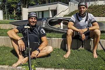 Hannes Aigner und Sideris Tasiadis sitzen vor einem Kanu. - Ein Klick auf das Bild führt zur vergrößerten Fotoansicht.