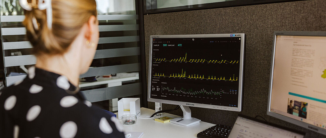 Frau sitzt an einem Schreibtisch und betrachtet Wellen auf dem Bildschirm eines PCs.