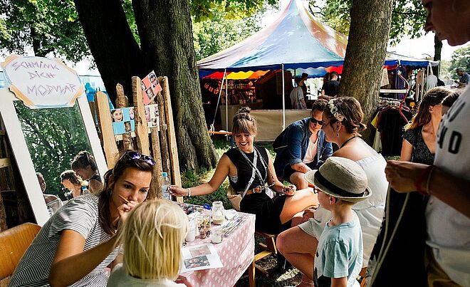 Mehrere Personen auf dem Modular-Festival in Augsburg 2019. Im Vordergrund ist ein Schminkstand zu sehen.