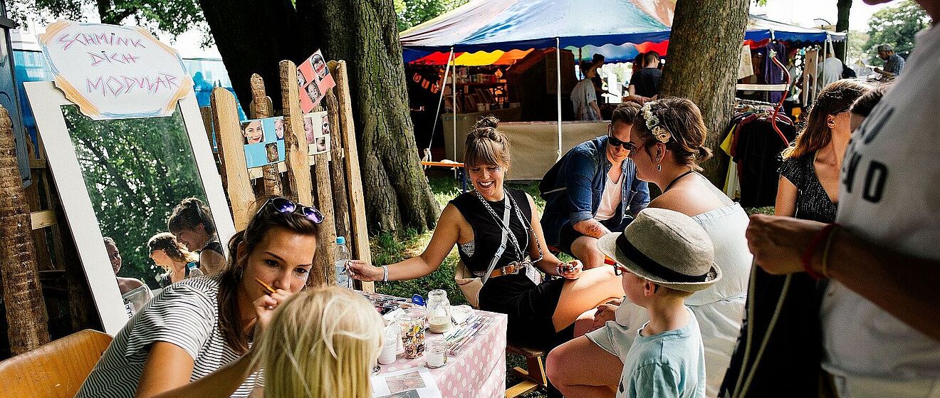 Mehrere Personen auf dem Modular-Festival in Augsburg 2019. Im Vordergrund ist ein Schminkstand zu sehen.