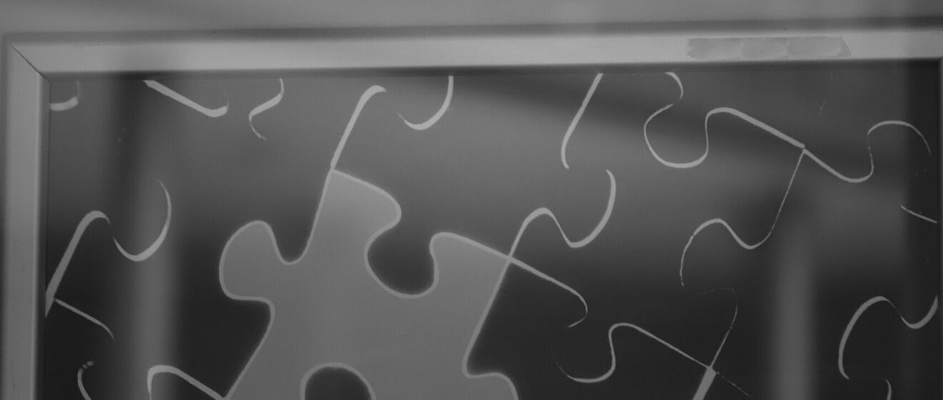 Darstellung eines Puzzles in einem Bilderrahmen mit dunkelgrauen Teilen und einem hellgrauen Puzzleteil.