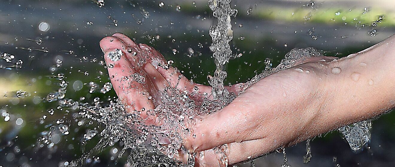 Hand unter einem laufenden Wasserhahn.