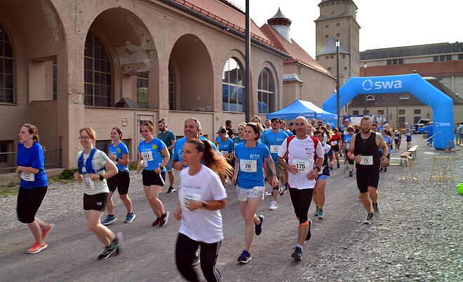 Läufer mit swa Trikot laufen beim swa Spendenlauf. Im Hintergrund ist das Ziel mit swa Branding