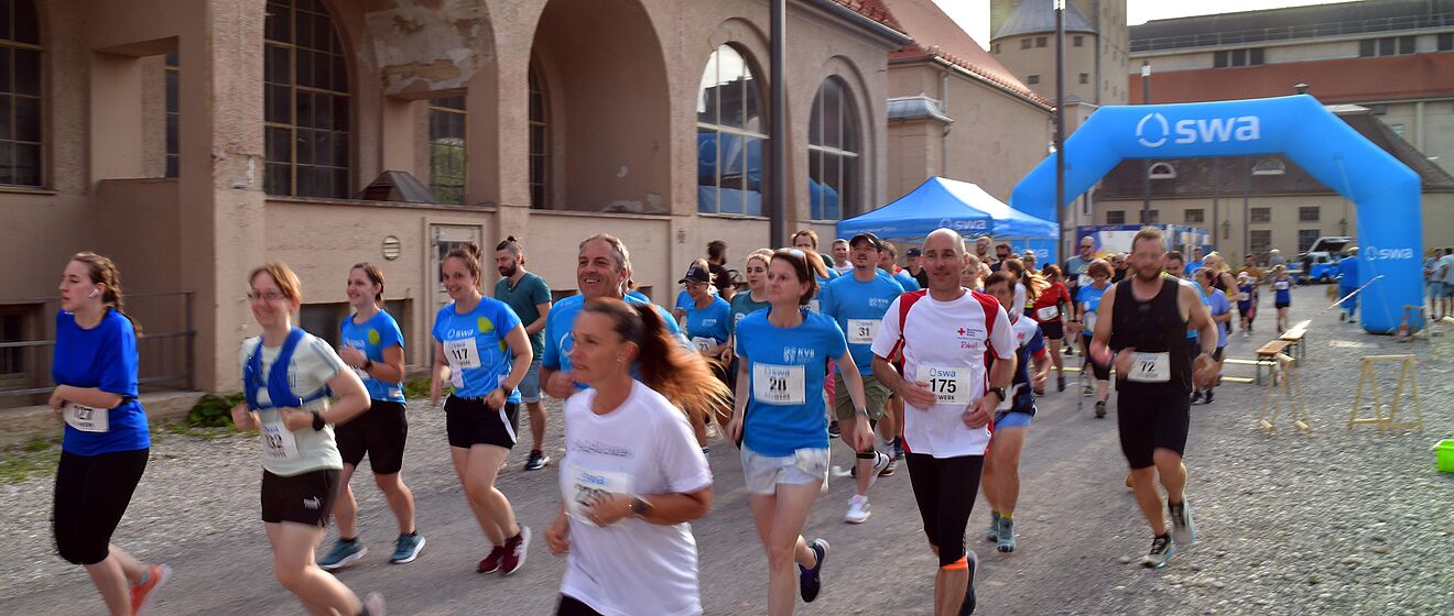 Läufer mit swa Trikot laufen beim swa Spendenlauf. Im Hintergrund ist das Ziel mit swa Branding