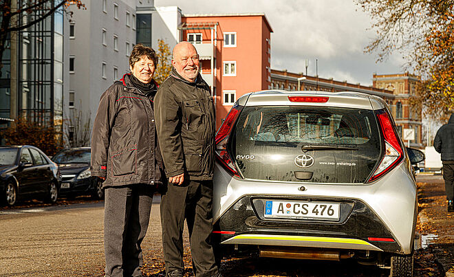 Ein Mann und eine Frau stehen hinter einem Carsharing Auto